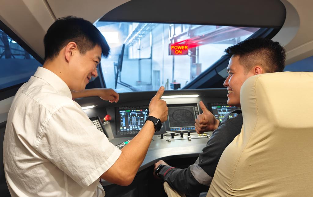 8月25日，在印度尼西亞萬隆的雅萬高鐵德卡魯爾動車所內(nèi)，中國師傅穆振（左）在向印尼火車司機塞蒂亞萬講解動車組出庫前的上電作業(yè)。